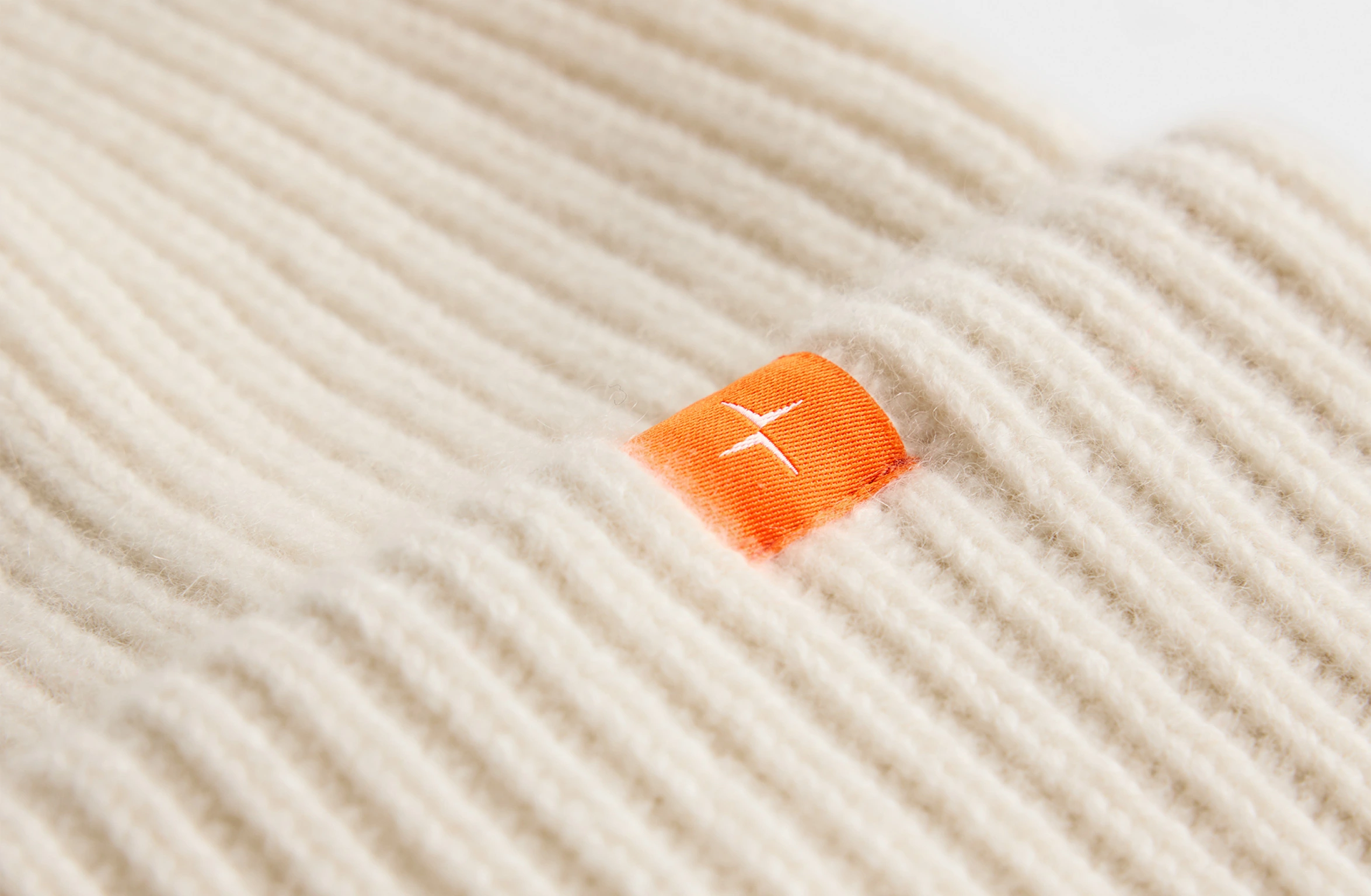 Beige strikket kasjmirlue med en liten oransje Polestar-detalj