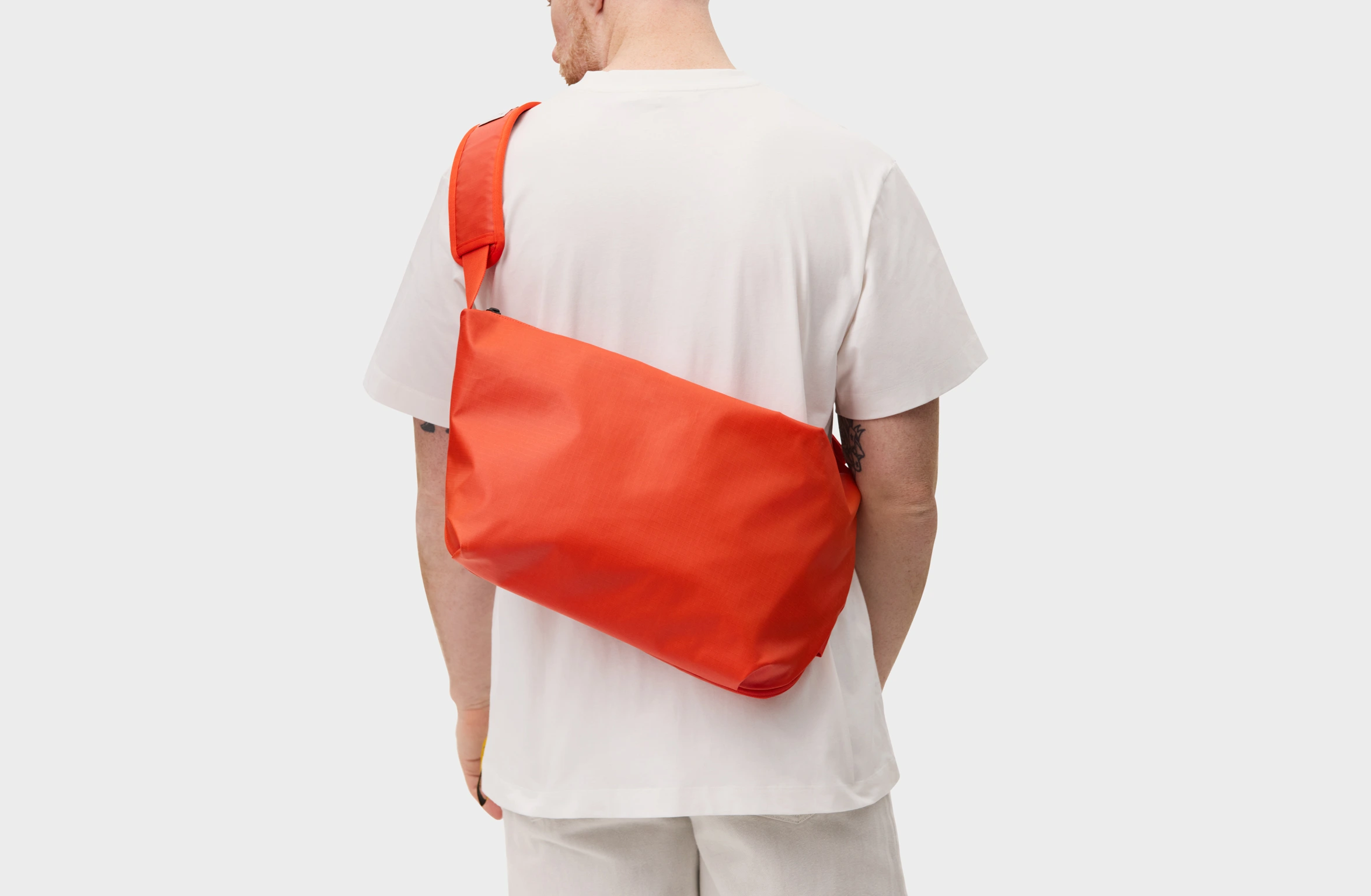 Red sling bag with an adjustable strap and a branded label on the shoulder pad.