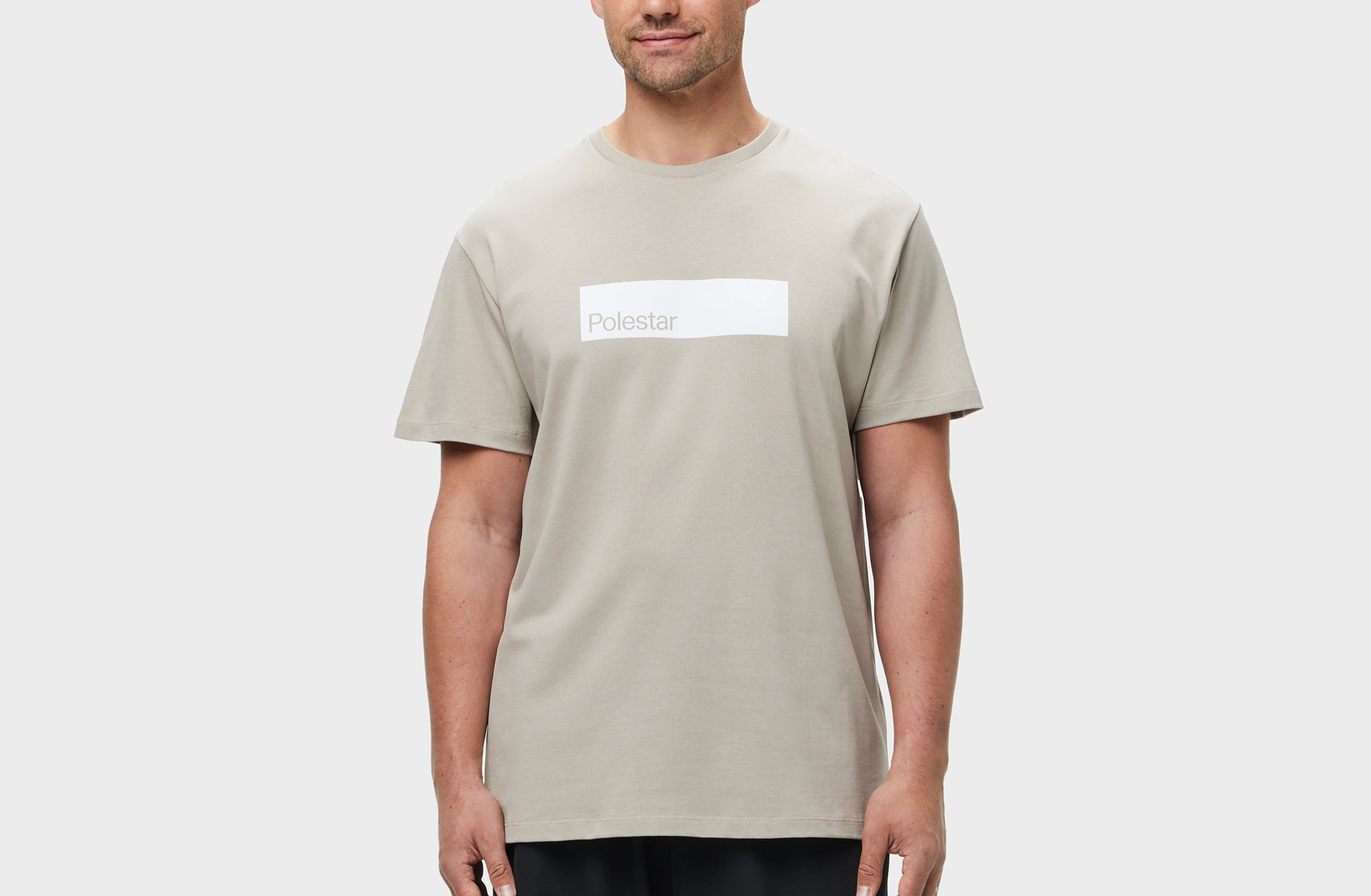 Beige T-skjorte med hvit rektangulær grafikk på brystet, med Polestar-ordmerket i en annen hvit fargetone.