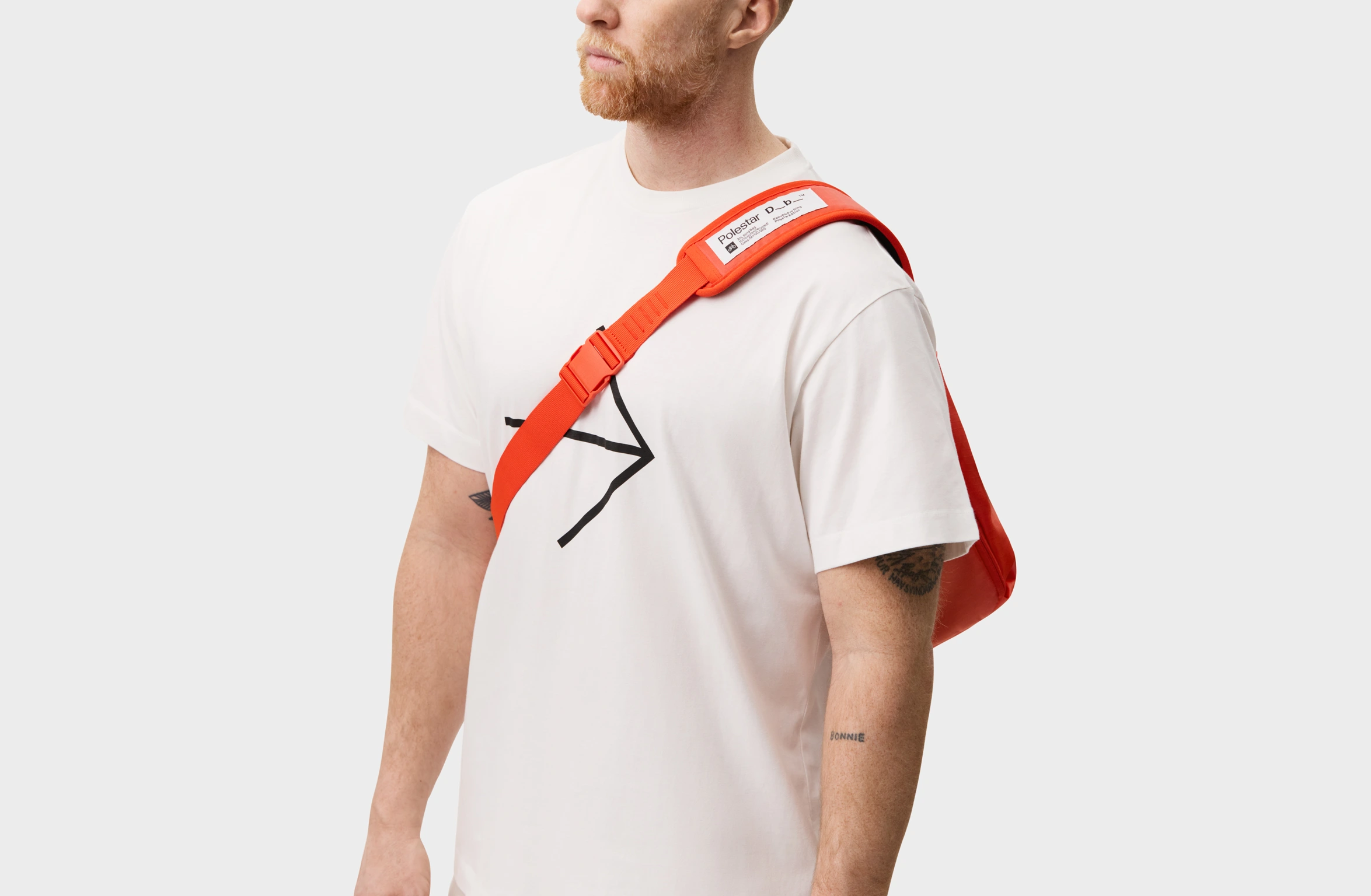 Red sling bag with an adjustable strap and a branded label on the shoulder pad.