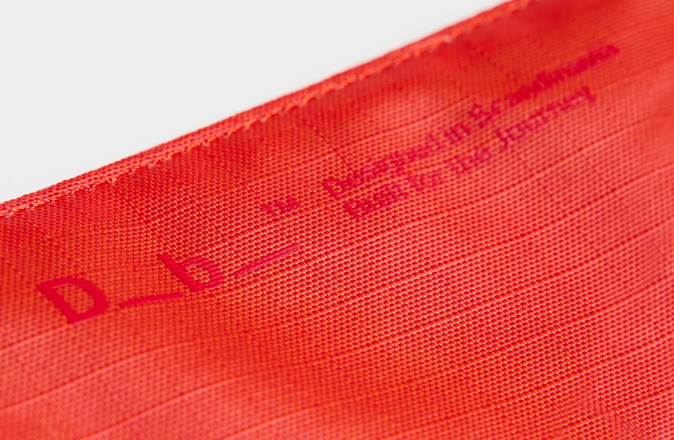 Red sling bag with an adjustable strap and a branded label on the shoulder pad.