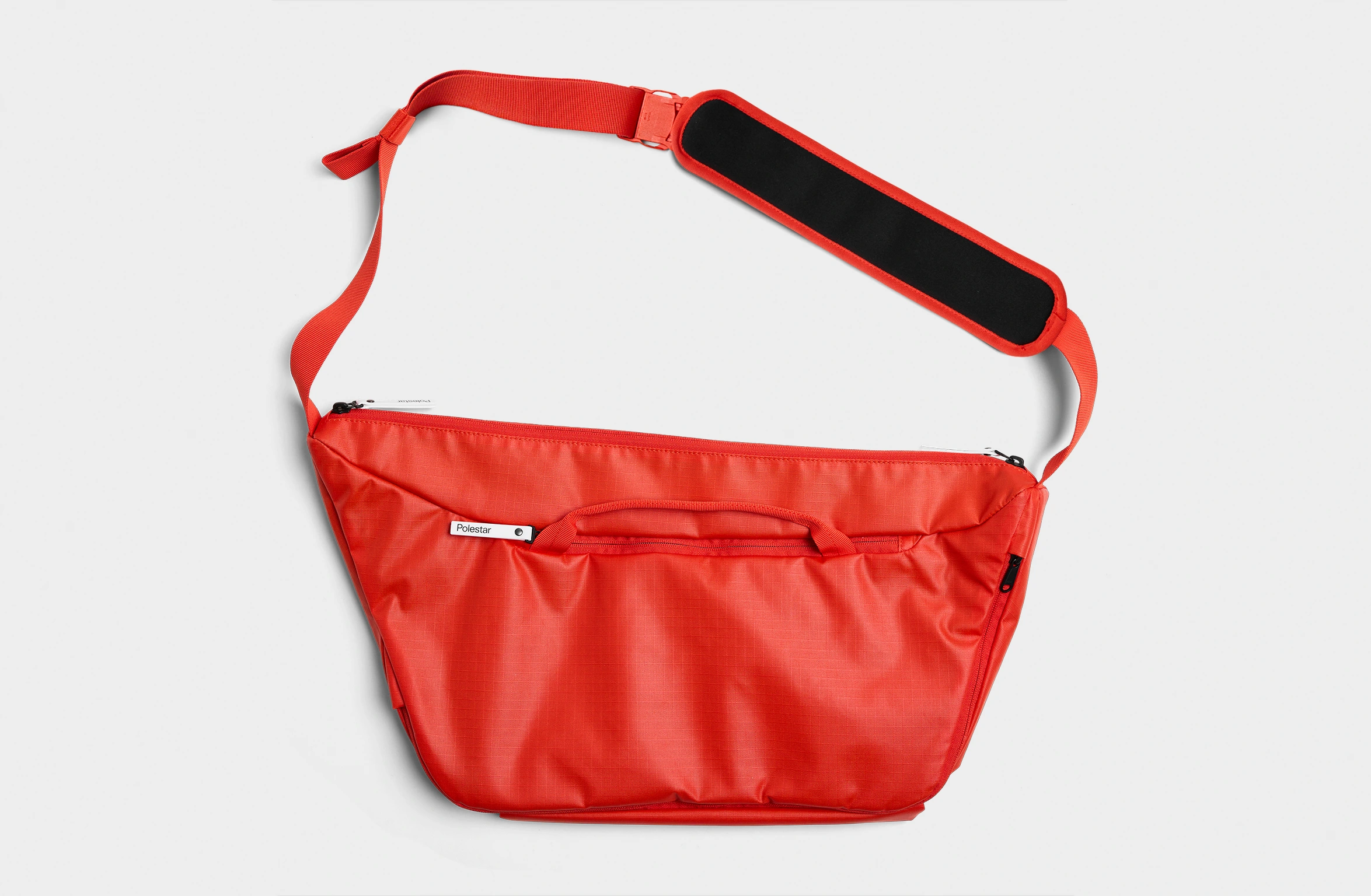 Rød sling bag med justerbar rem og et mærke på skulderpuden.